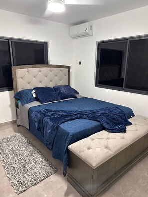 Een slaapkamer met een bed, nachtkastje, vloerkleed en raam.