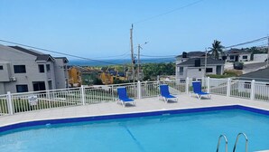 A swimming pool with a white fence, blue lounge chairs, and a view of the ocean. - Cozy 2-bedroom bungalow with AC in charming Runaway Bay. Hosts up to 4  persons. (Runaway Bay)