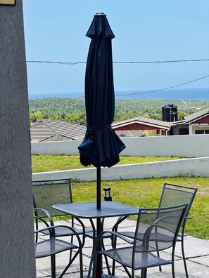 Een terras met een tafel, stoelen, een parasol en uitzicht op een landschap met gebouwen en een waterpartij.