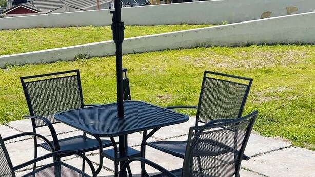 A patio with a table and chairs under a large umbrella, overlooking a residential area with houses and a view of the ocean. - Cozy 2-bedroom bungalow with AC in charming Runaway Bay. Hosts up to 4  persons. (Runaway Bay)