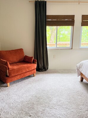 A room with a red sofa, a bed with a striped cover, a window with a view of greenery, and a curtain. - Cedar House on Highland Trail + Sleeps 14 +  Spacious Cottage Retreat (Stanwood)
