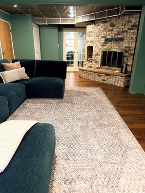 Ein Wohnzimmer mit einem Ecksofa, einem gemusterten Teppich und einem Kamin aus Ziegelsteinen.