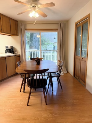 A dining area with a wooden table and chairs, a ceiling fan, and a view through a window. - Cedar House on Highland Trail + Sleeps 14 +  Spacious Cottage Retreat (Stanwood)
