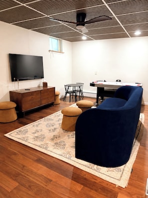 Ein modernes Wohnzimmer mit Flachbildfernseher, Holzschrank, blauem Sofa und Esstisch mit Stühlen.