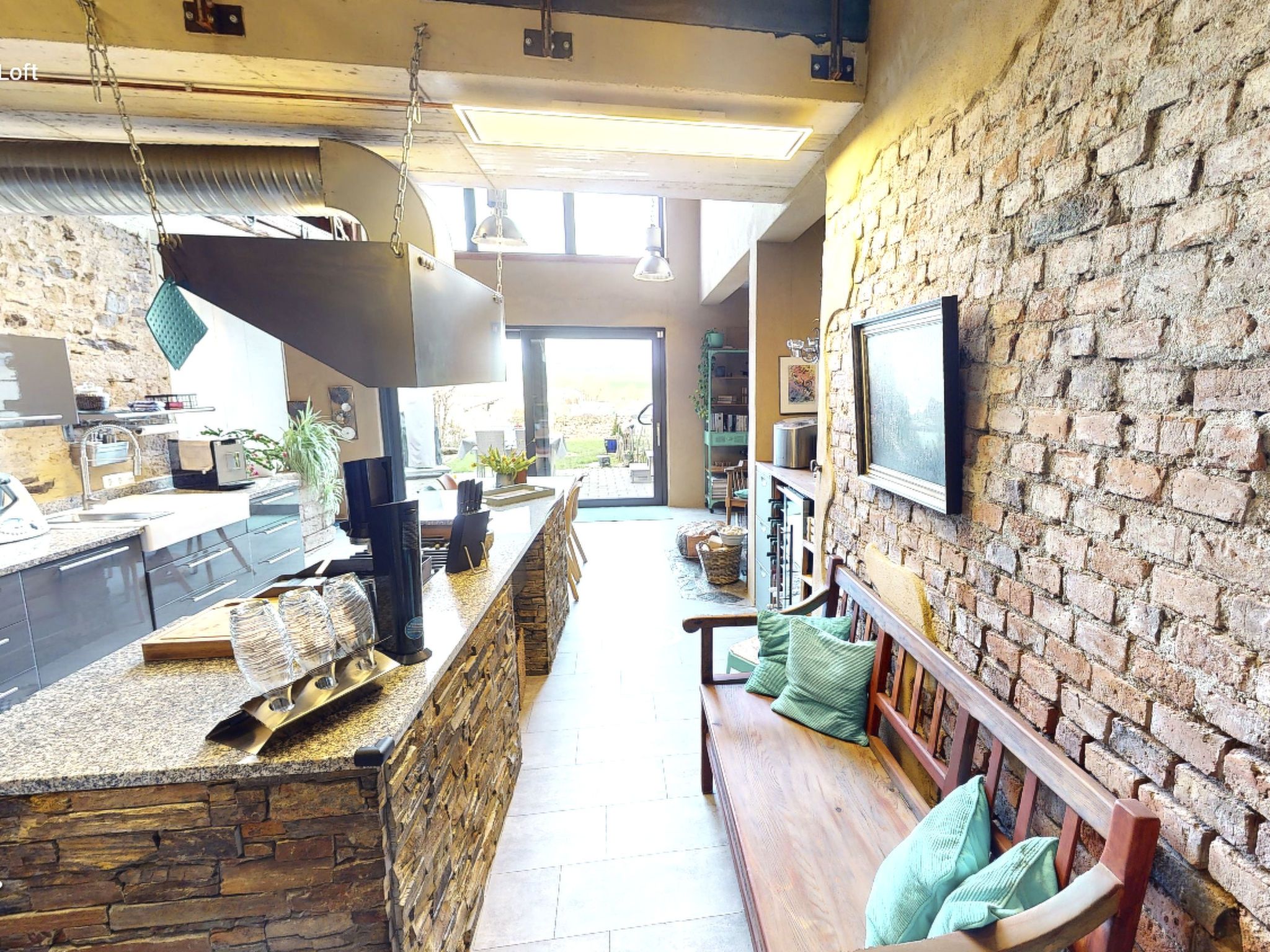 A kitchen with a stone counter, a hanging light fixture, and a view of the outdoors.