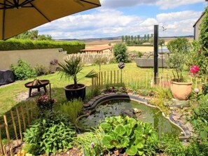 A garden with a pond, potted plants, a wooden bench, and a fence. - Maifelder Wellness-Loft in Gappenach by Interhome (Gappenach)