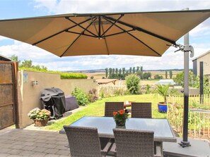 An outdoor patio with a table and chairs, a barbecue grill, and a large umbrella. - Maifelder Wellness-Loft in Gappenach by Interhome (Gappenach)