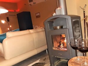 A room with a white sofa, a wood-burning stove, and two glasses of red wine on a table. - Maifelder Wellness-Loft in Gappenach by Interhome (Gappenach)