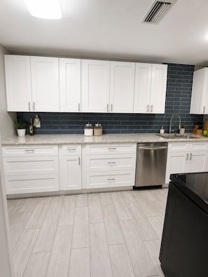 A modern kitchen with white cabinets, a black tiled backsplash, and a stainless steel dishwasher.