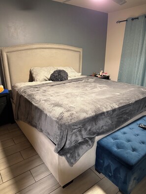 A bed with a headboard, a bedside table with a lamp, and a blue bench.