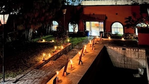 A building with a stone pathway leading to a door, surrounded by trees and lit by candles. - Escápa de la realidad, casita en el cerro campestre con el mejor clima! (Tepic)