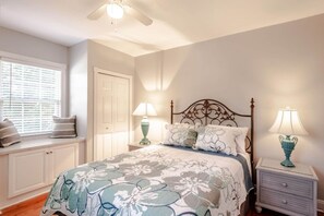 A bedroom with a bed, two bedside lamps, a window with blinds, a door, and a ceiling fan. - Sunny Summerville Court Condos (Mobile)