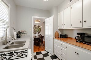 A kitchen with white cabinets, a wooden countertop, a stove, and a coffee maker. - Sunny Summerville Court Condos (Mobile)