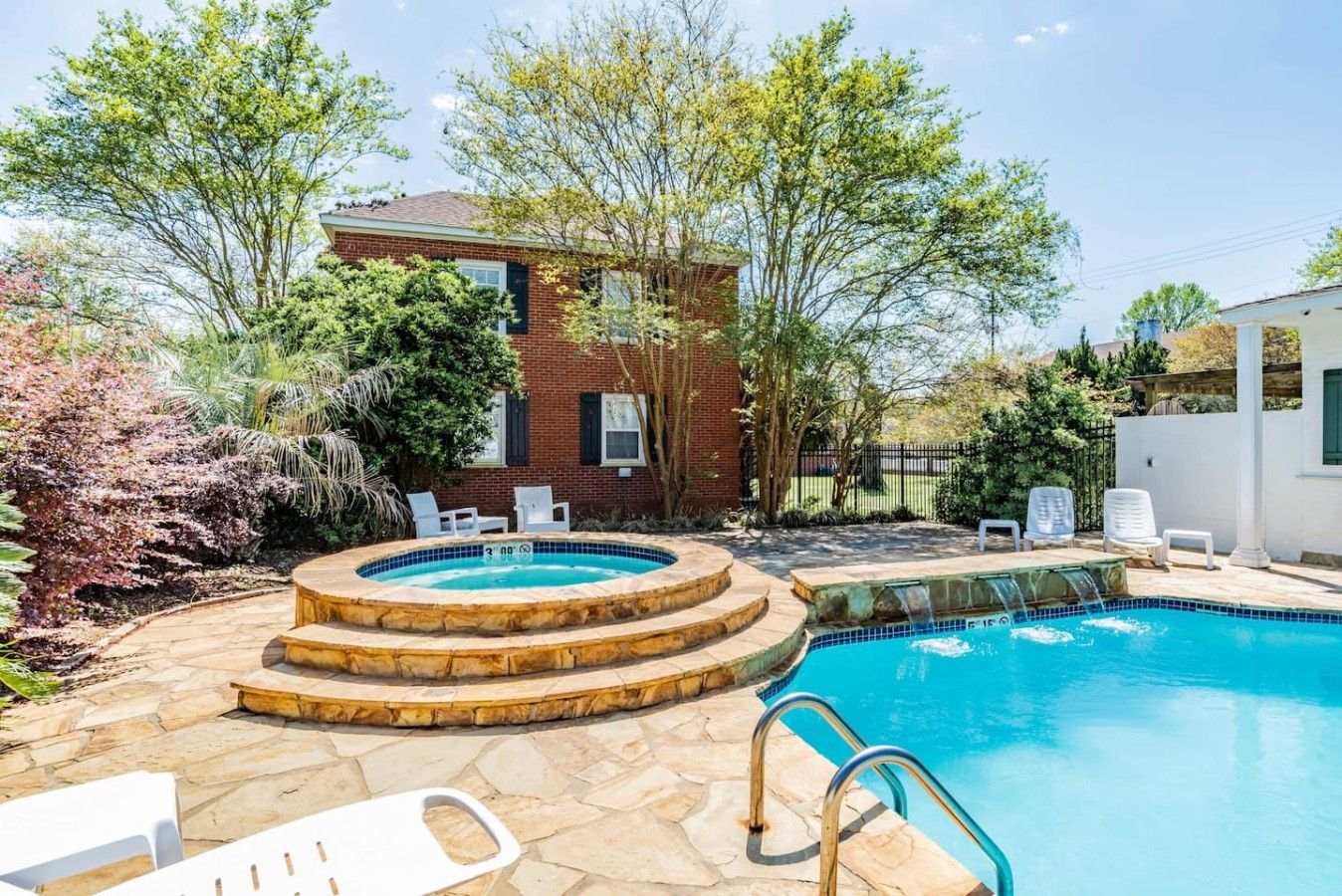 Un jardin avec une piscine, des marches en pierre et des chaises longues blanches.