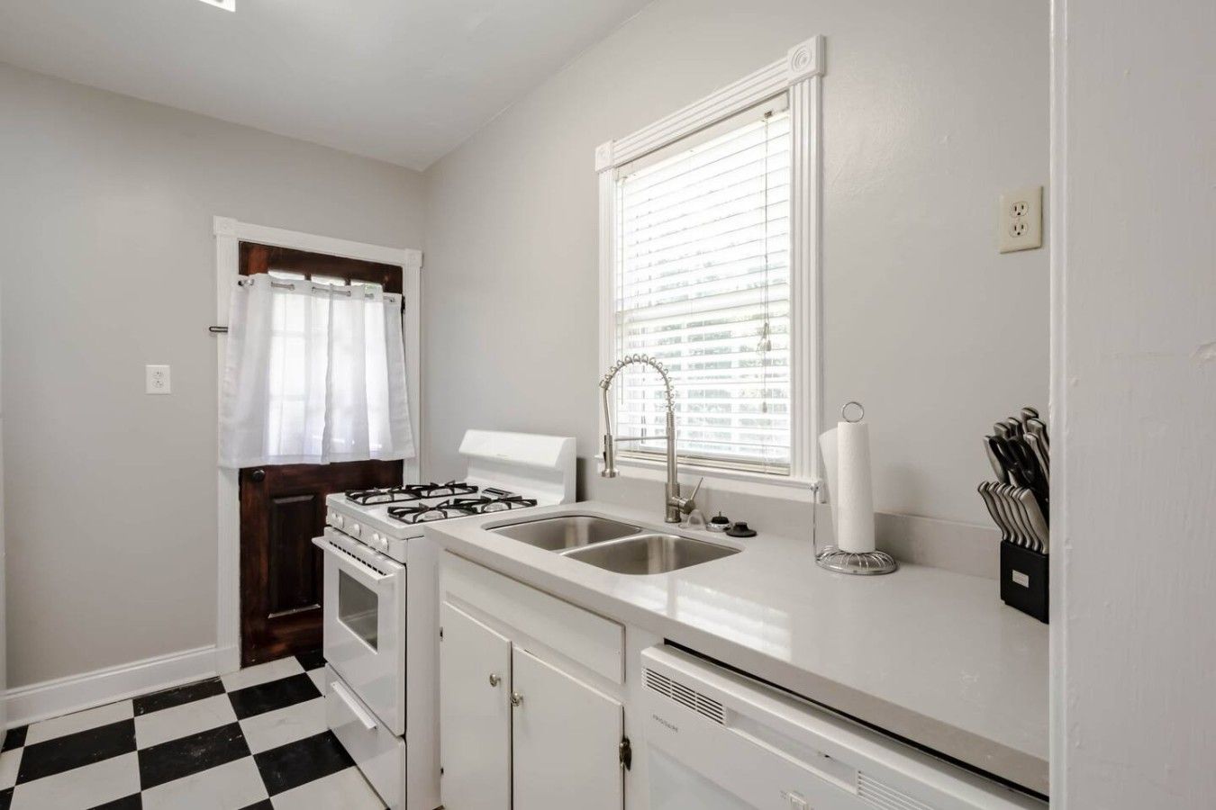 A kitchen with a gas stove, sink, and a window with blinds.