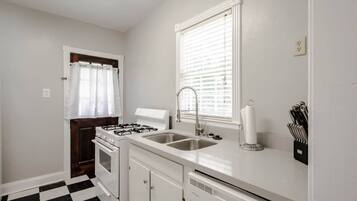 A kitchen with a gas stove, sink, and a window with blinds.