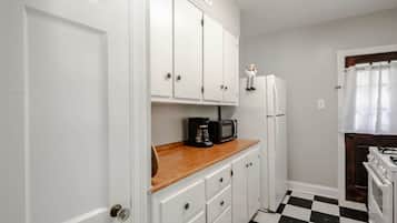 Una cocina compacta con gabinetes blancos, encimera de madera, cafetera negra, refrigerador blanco y piso a cuadros.