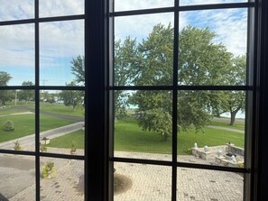 A view through a window with a grid pattern, a paved area with planters, and a grassy field with trees.