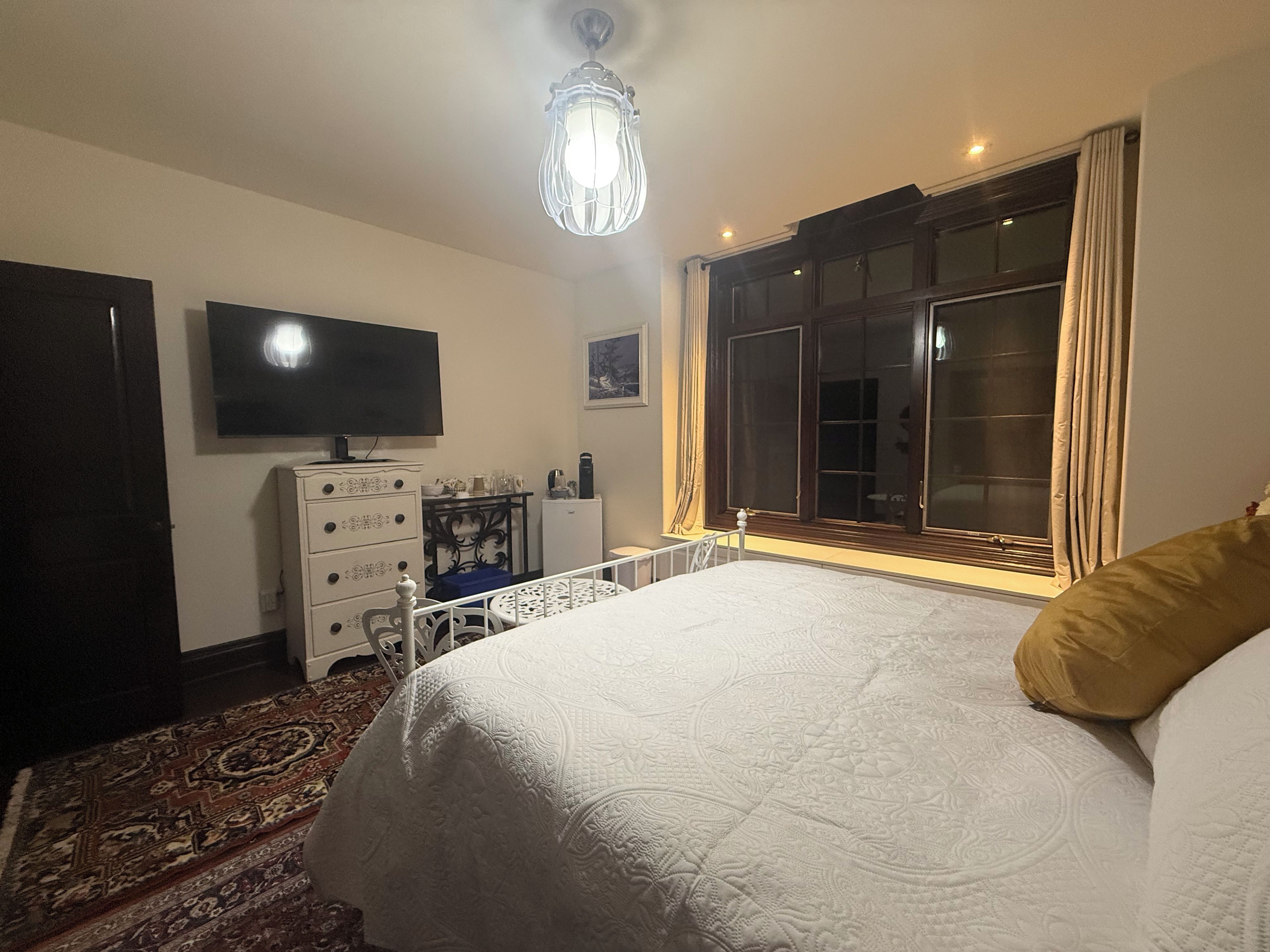 A bedroom with a bed, dresser, television, and a window with curtains.