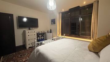 A bedroom with a bed, dresser, television, and a window with curtains.