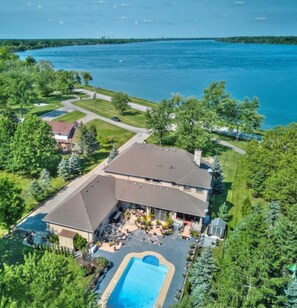 A large building with a swimming pool, surrounded by greenery and a body of water.
