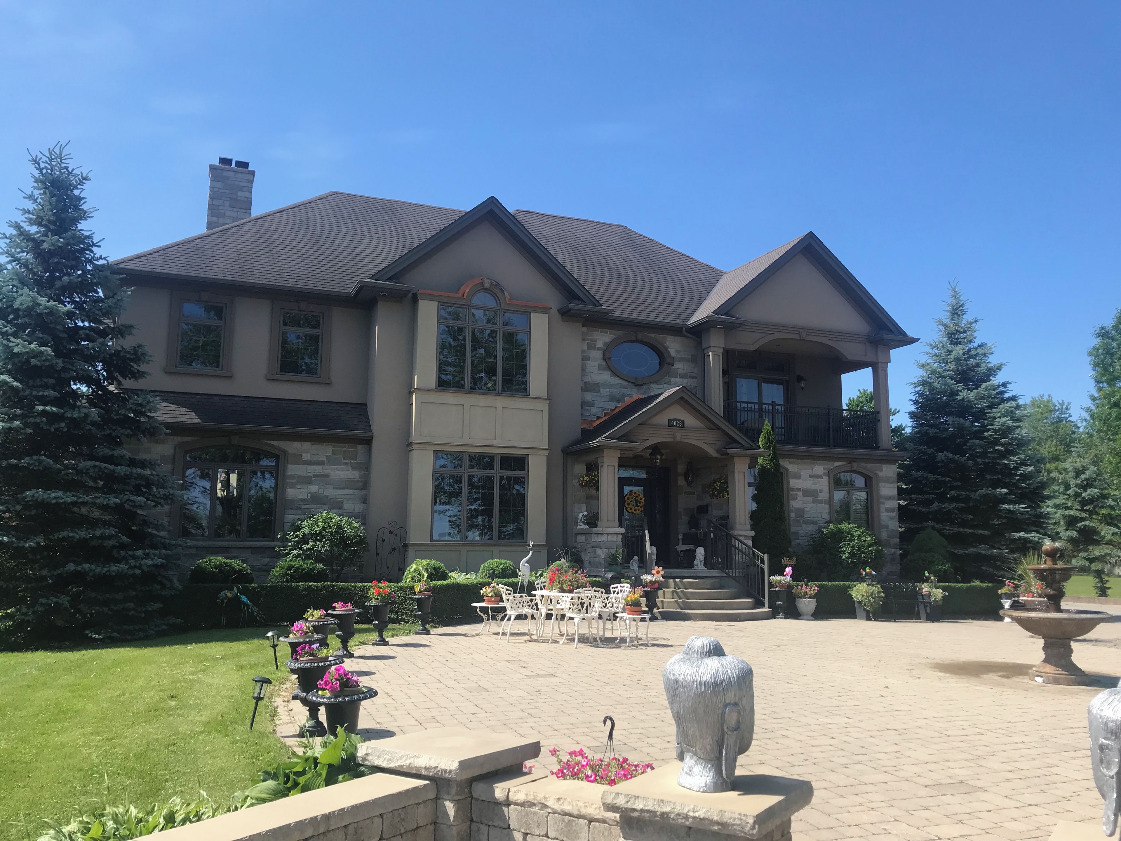 A large two-story house with a stone facade, multiple windows, and a front porch with outdoor seating.