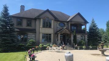 A large two-story house with a stone facade, multiple windows, and a front porch with outdoor seating.