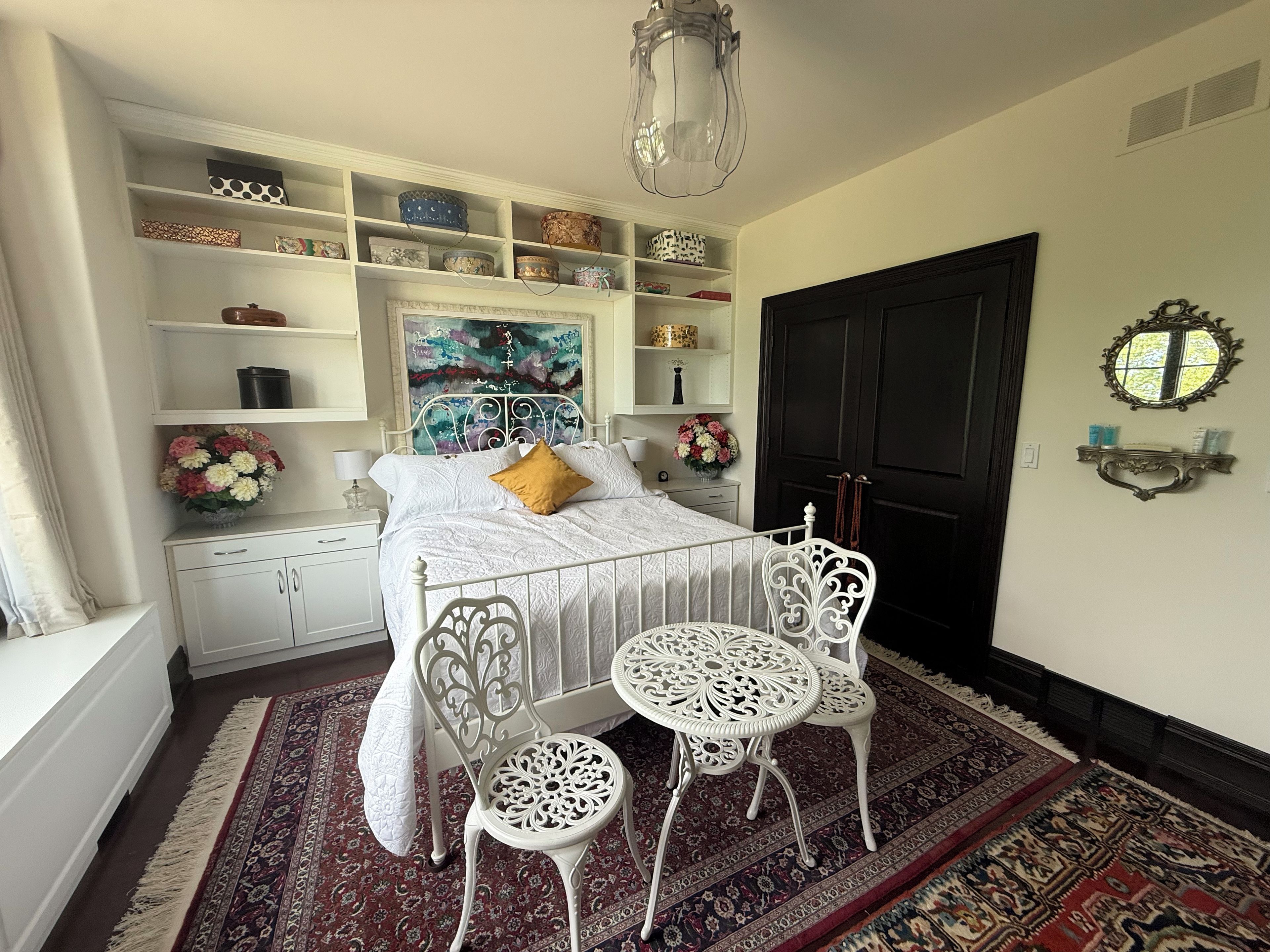 A bedroom with a bed, bedside tables, a nightstand, a decorative mirror, a patterned rug, and a door.