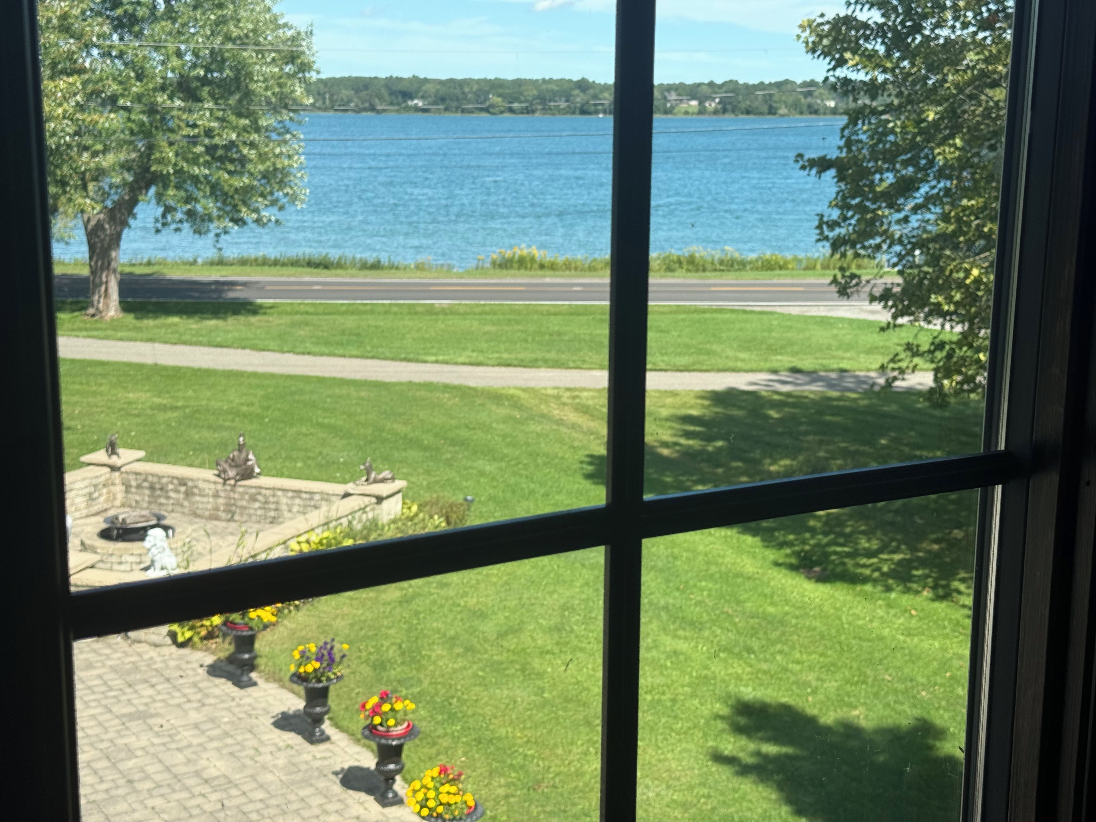 A view through a window of a grassy area with a body of water, a paved path, and a statue.