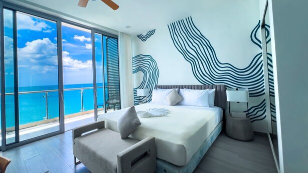 A modern hotel room with a large bed, a seating area, a ceiling fan, and a view of the ocean. - The Tides - Oceanfront King Suite (Montego Bay)