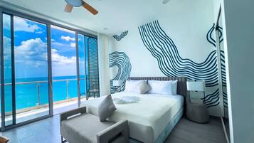 A modern hotel room with a large bed, a seating area, a ceiling fan, and a view of the ocean.