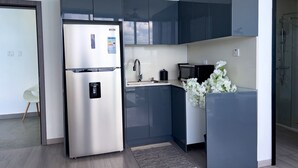 A modern kitchen with a stainless steel refrigerator, dark cabinets, a sink, and a microwave. - The Tides - Oceanfront King Suite (Montego Bay)