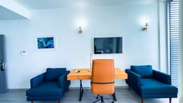 Een moderne kamer met een bureau, twee blauwe banken, een oranje bureaustoel, een flatscreen-tv en wandlampen.
