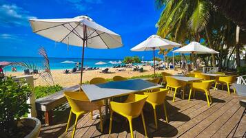 A beachside patio with yellow chairs and white umbrellas, overlooking a sandy beach and the ocean.