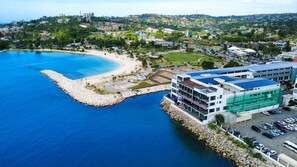 Una zona costera con playa, un puerto deportivo y un edificio con estacionamiento.