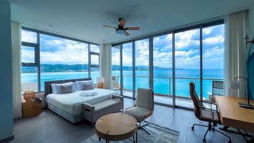 A modern hotel room with a large bed, two chairs, a desk, and a view of the ocean.