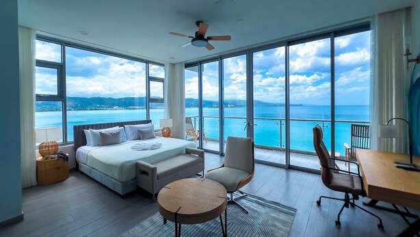 Quarto de hotel moderno com uma cama grande, duas cadeiras, uma escrivaninha e vista para o oceano.