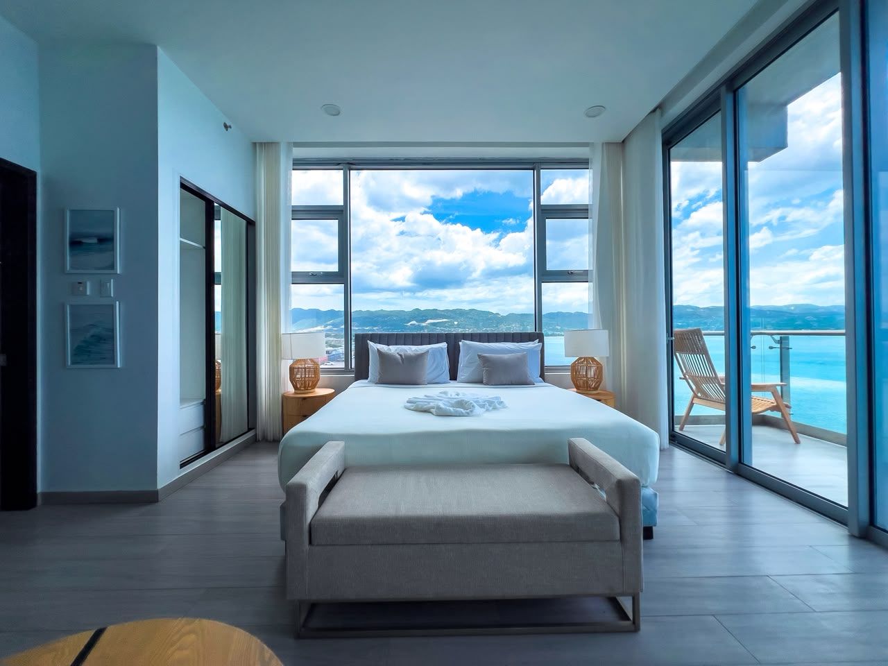 A modern bedroom with a large bed, a view of the sea, and a balcony with a chair.