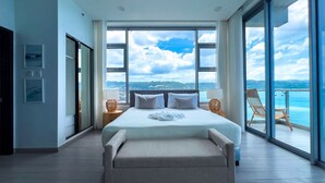 Quarto moderno com uma cama grande, vista para o mar e uma varanda com uma cadeira.