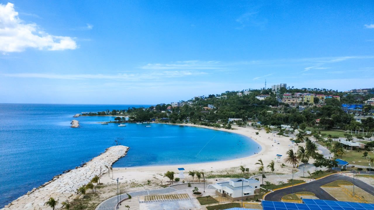 A coastal area with a beach, a rocky shoreline, and buildings in the background.