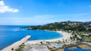 Uma área costeira com praia, falésias rochosas e edifícios ao fundo.