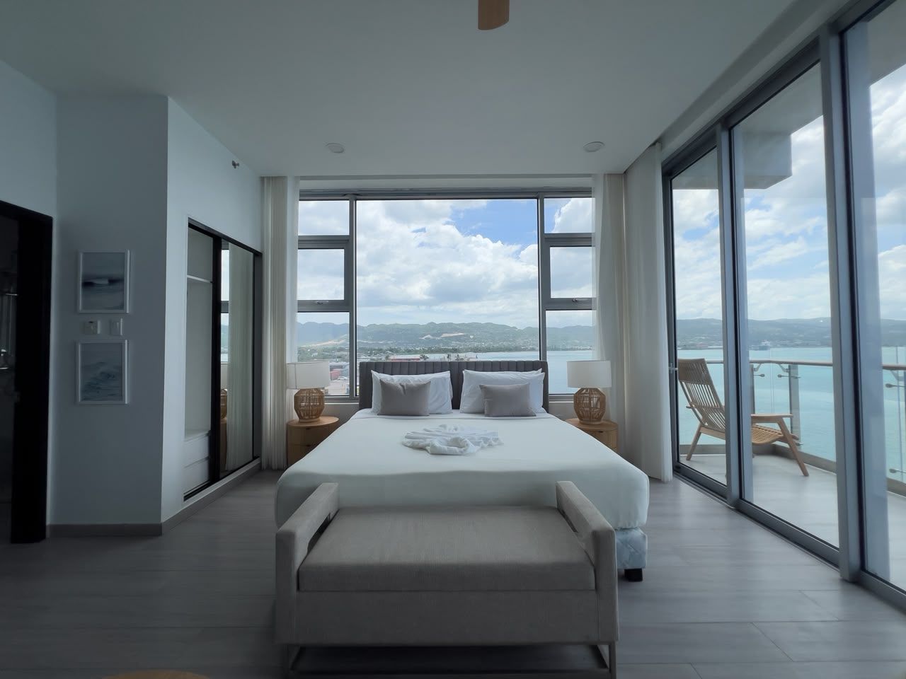 A spacious bedroom with a large bed, a balcony with a view of the sea, and a sliding door leading to another room.