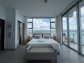 Un dormitorio amplio con una cama grande, un balcón con vistas al mar y una puerta corrediza que da a otra habitación.