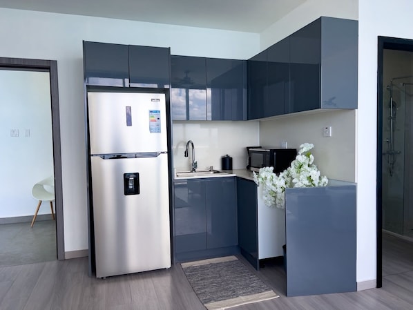 A modern kitchen with a stainless steel refrigerator, dark cabinets, a sink, and a microwave.
