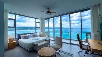 A modern hotel room with a large bed, a desk, a chair, and a view of the sea.