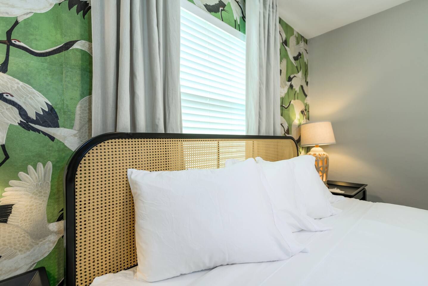 A hotel room with a bed, a nightstand with a lamp, and a window with blinds.