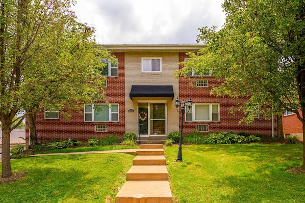 A two-story brick building with a front door, a small porch, and a pathway leading to the entrance.