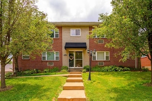 A two-story brick building with a front door, a small porch, and a pathway leading to the entrance.
