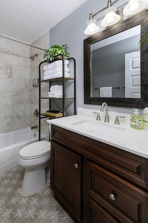 A bathroom with a white toilet, a bathtub, a vanity with a mirror, and a towel rack with folded towels.