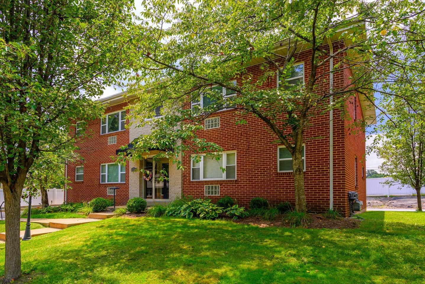 A two-story brick building with a front entrance, a small porch, and a well-maintained lawn.